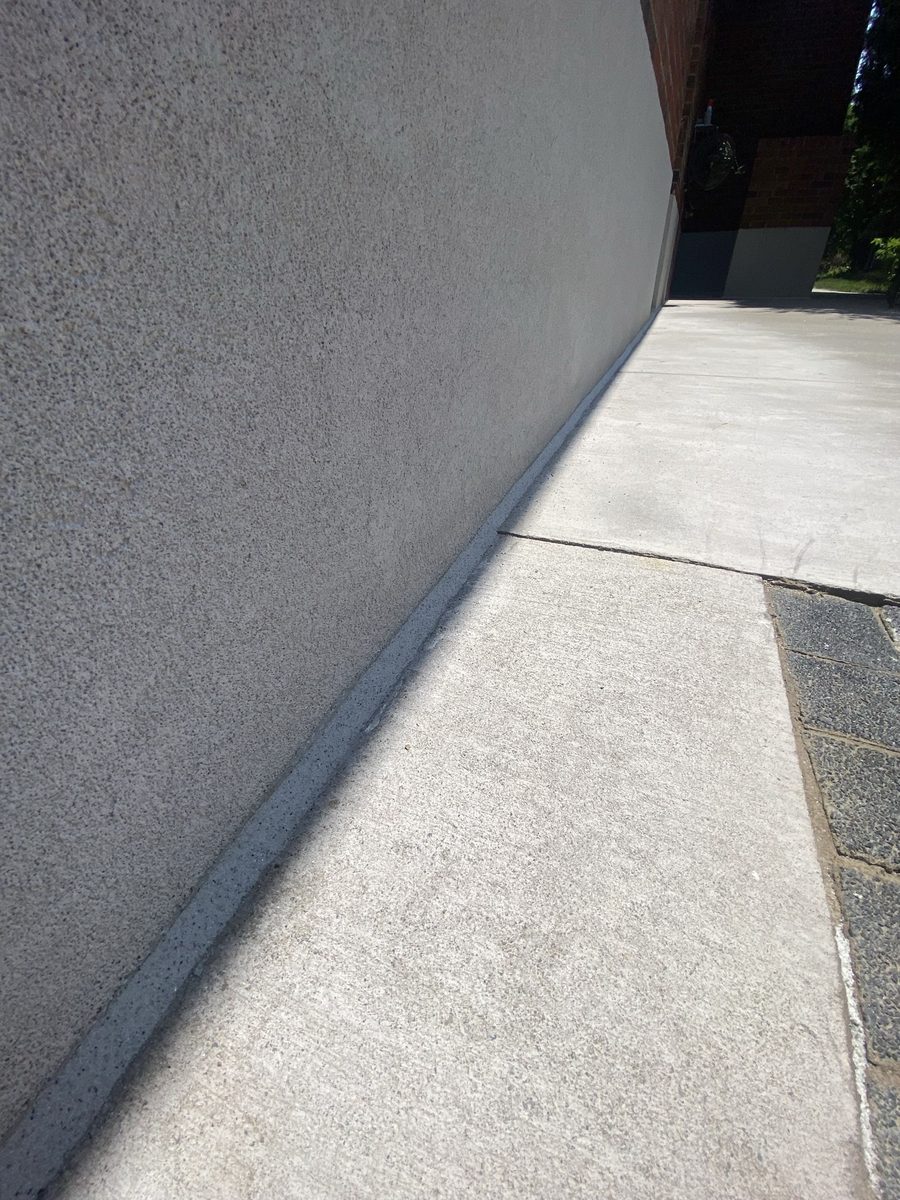 Stucco wall to walkway — the long slab-to-wall joint sealed in a matching grey