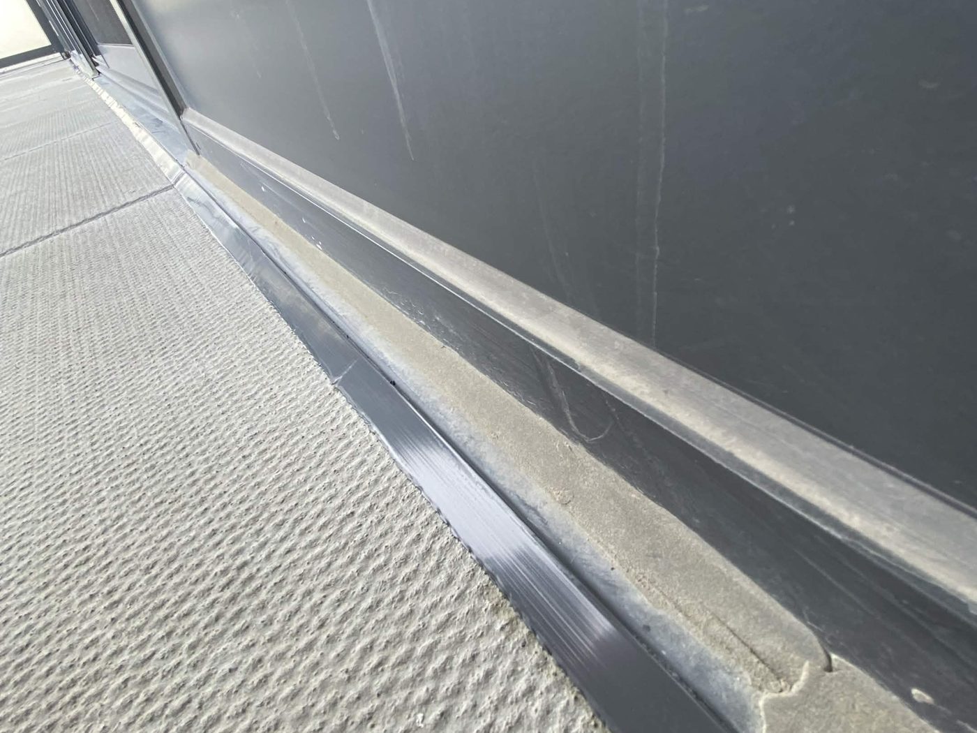 A door frame sealed to the paving stones at its base — a clean grey bead along the whole threshold