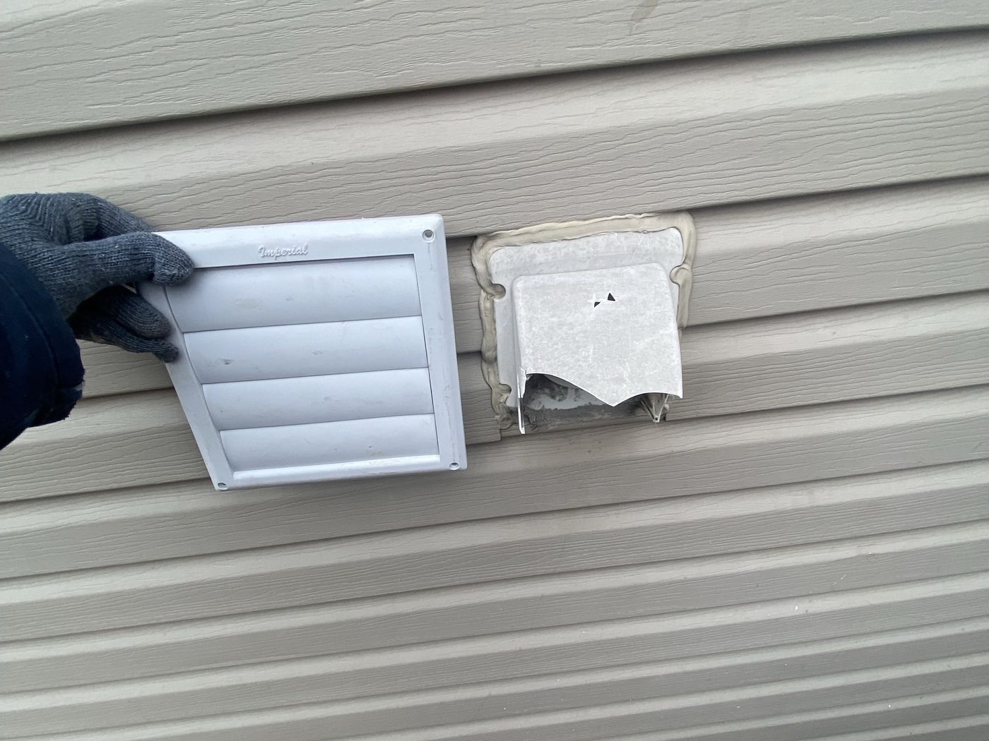 Two exhaust vents on siding — the new hood beside the old cover it is replacing