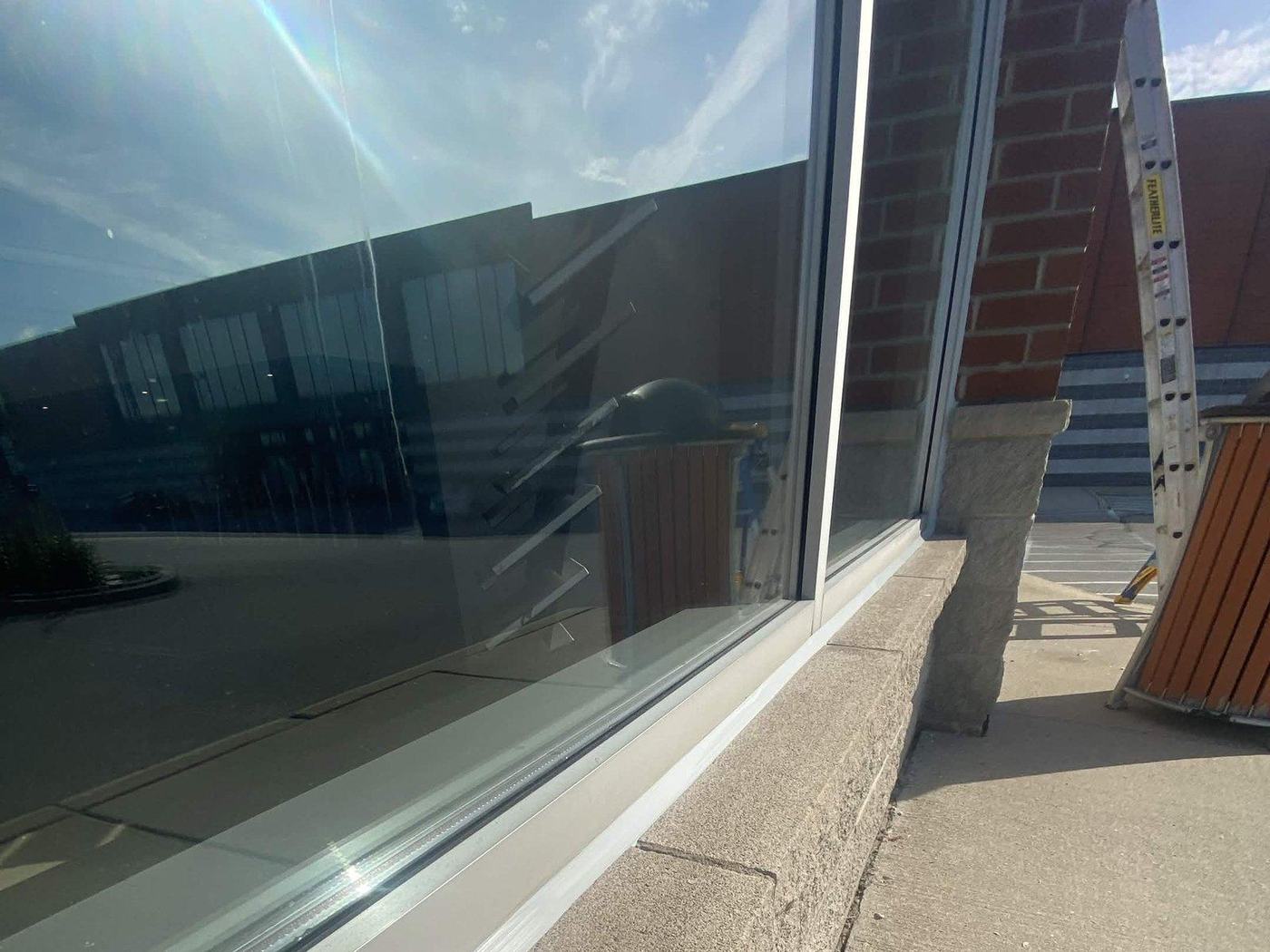 A long window sill freshly resealed — a continuous silicone bead tooled along the full length of the glazing line, with a ladder still set up alongside.