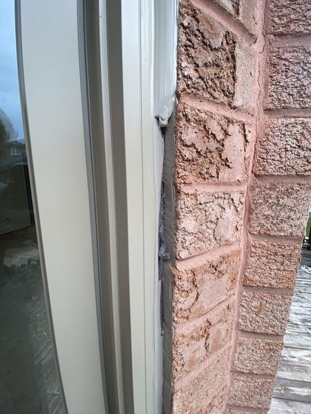 Another contractor's prep: a brick window frame with the old silicone only partly scraped off and bare foam showing in the joint