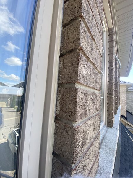 Royal Caulking prep: a brick window frame with every trace of the old sealant cut out, leaving a clean open joint between frame and brick