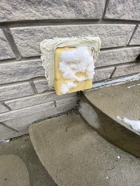 Before: Dryer vent on stone — the foam-stuffed hole replaced with a hood, sealed at the flange